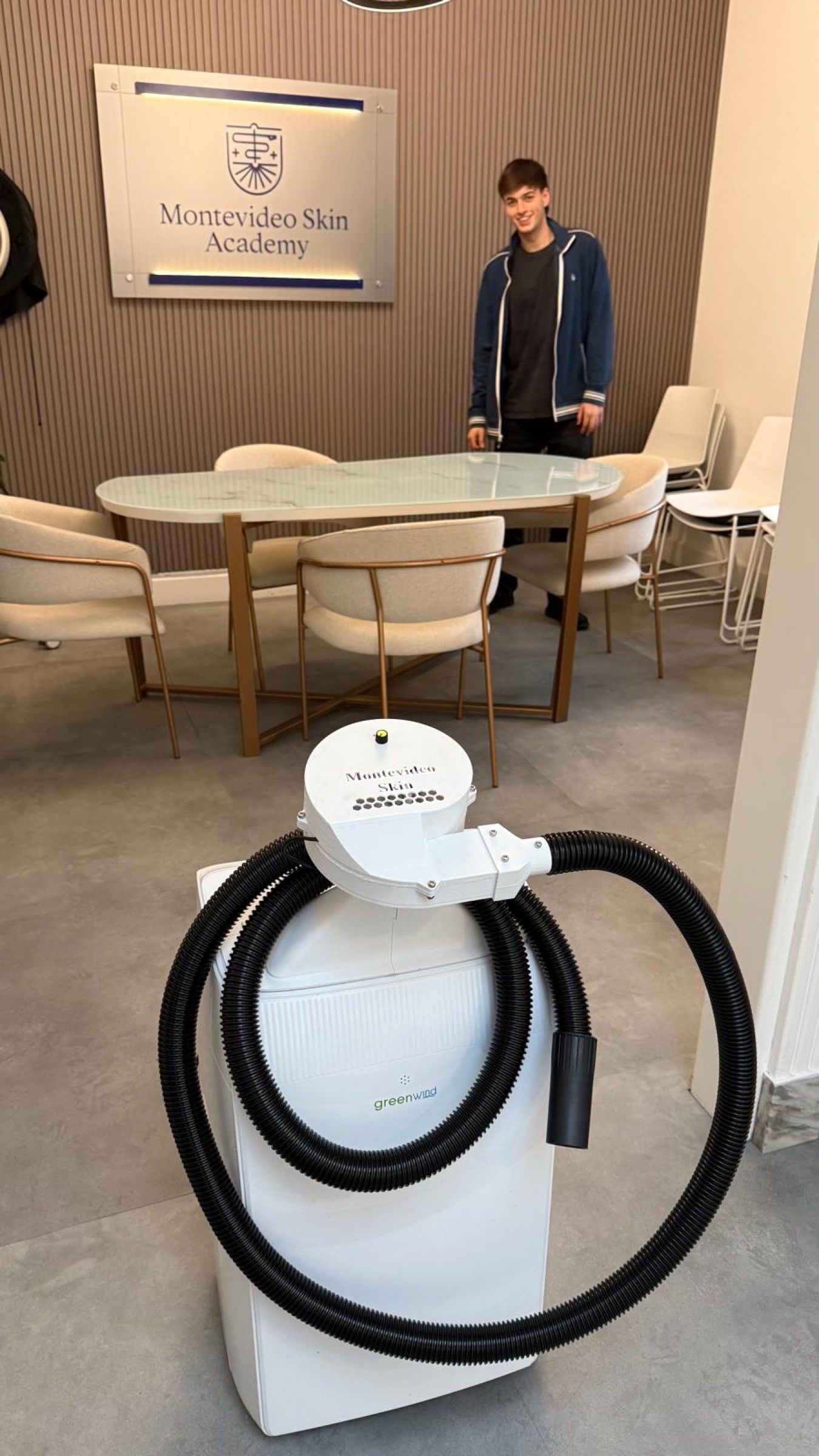Equipo de refrigeración blanco con una turbina blanca y una manguera negra enrollada, en una sala de Montevideo Skin Academy; al fondo, una persona de pie.